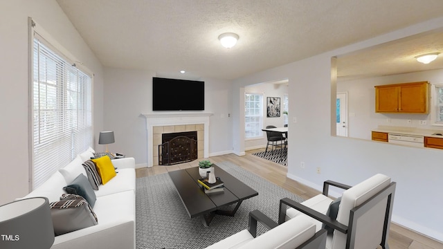 living room with a textured ceiling, light hardwood / wood-style flooring, a wealth of natural light, and a tiled fireplace