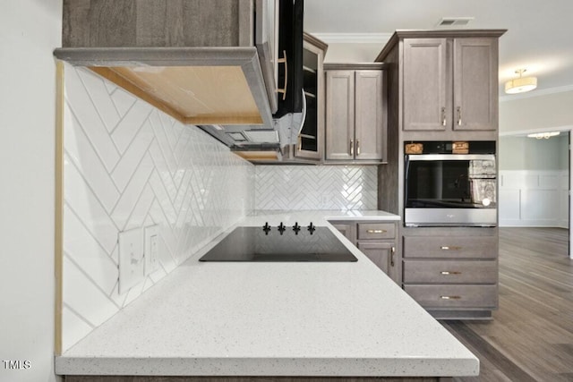 kitchen featuring crown molding, tasteful backsplash, dark hardwood / wood-style flooring, black electric stovetop, and oven