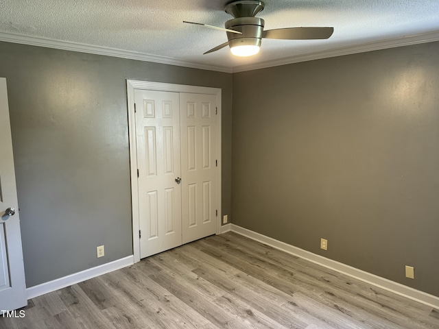 unfurnished bedroom with crown molding, ceiling fan, light wood-type flooring, a textured ceiling, and a closet