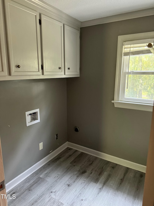 clothes washing area with cabinets, hookup for a washing machine, a textured ceiling, crown molding, and light hardwood / wood-style flooring