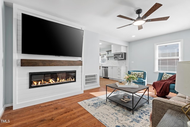 living room with ceiling fan, a large fireplace, and light wood-type flooring