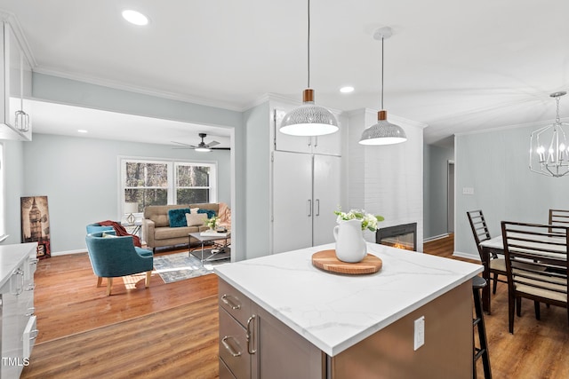 kitchen with pendant lighting, ceiling fan with notable chandelier, dark hardwood / wood-style floors, a fireplace, and a kitchen island