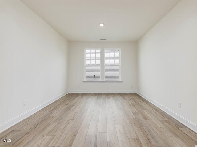 empty room with baseboards, visible vents, and light wood finished floors