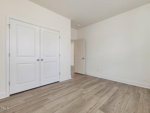 unfurnished bedroom featuring light wood-type flooring, a closet, and baseboards