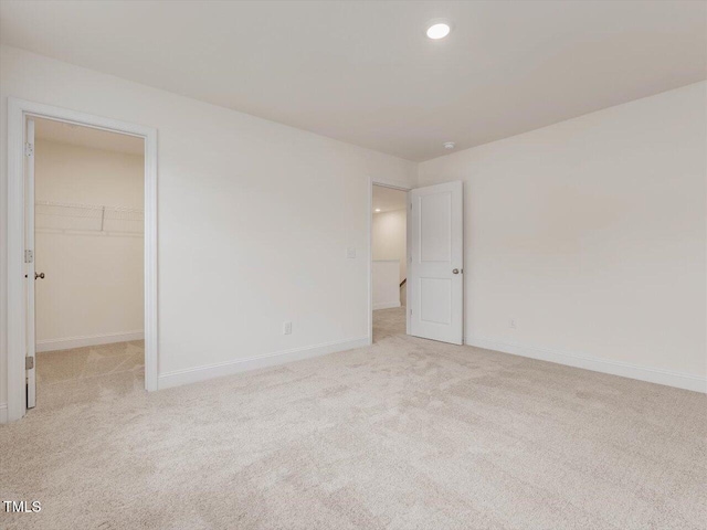 unfurnished bedroom with carpet, a spacious closet, baseboards, and recessed lighting