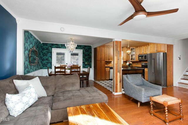 living room featuring french doors, ornamental molding, ceiling fan with notable chandelier, a textured ceiling, and light hardwood / wood-style flooring