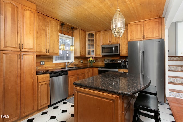 kitchen featuring a center island, dark stone counters, hanging light fixtures, sink, and appliances with stainless steel finishes