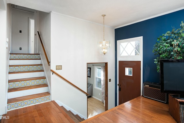 entrance foyer featuring a textured ceiling, light wood-type flooring, ornamental molding, and an inviting chandelier