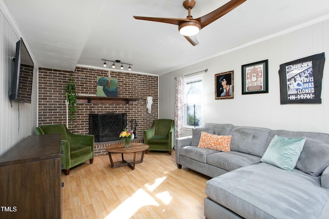 living room featuring ceiling fan, a brick fireplace, crown molding, track lighting, and hardwood / wood-style flooring