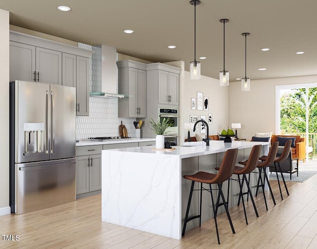 kitchen with a breakfast bar, a sink, gray cabinetry, appliances with stainless steel finishes, and wall chimney range hood