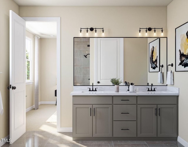 bathroom with a sink, baseboards, double vanity, and a tile shower