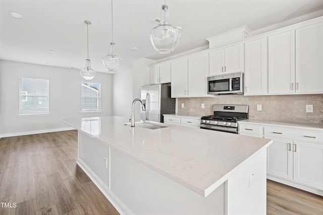 kitchen with backsplash, a center island with sink, light wood-style flooring, stainless steel appliances, and a sink