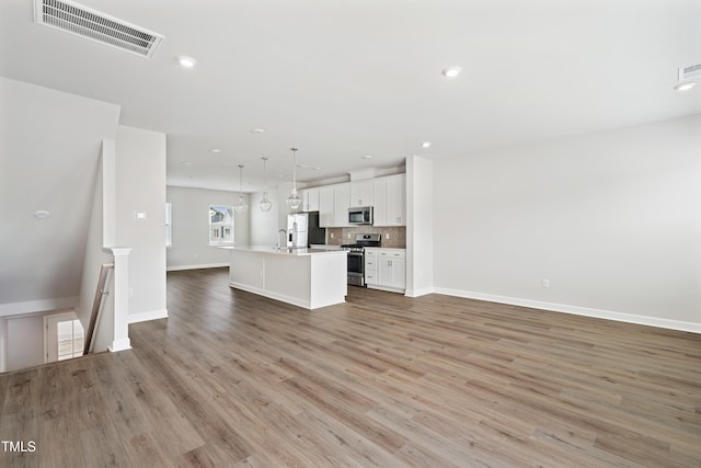 unfurnished living room with visible vents, baseboards, recessed lighting, light wood-style floors, and a sink