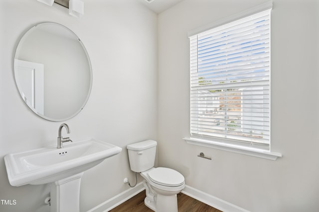 half bathroom with a sink, toilet, baseboards, and wood finished floors