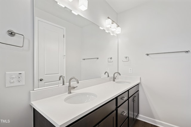 full bathroom featuring a sink, baseboards, wood finished floors, and double vanity