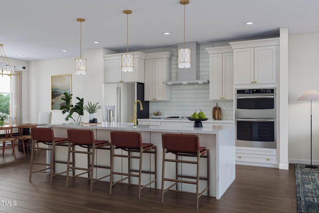 kitchen featuring wall chimney range hood, a center island with sink, light countertops, decorative backsplash, and stainless steel appliances