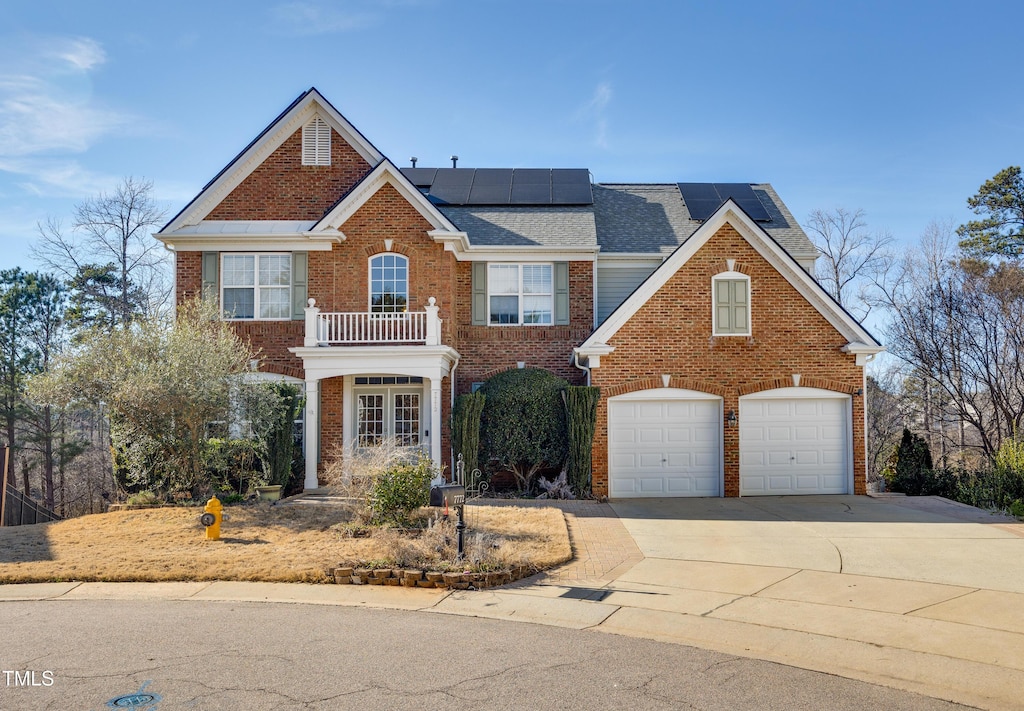 view of front of home featuring a balcony, driveway, roof mounted solar panels, and brick siding