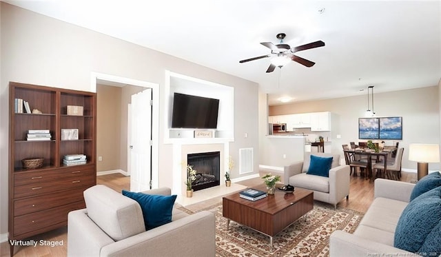 living area with visible vents, a ceiling fan, a fireplace with flush hearth, light wood-type flooring, and baseboards