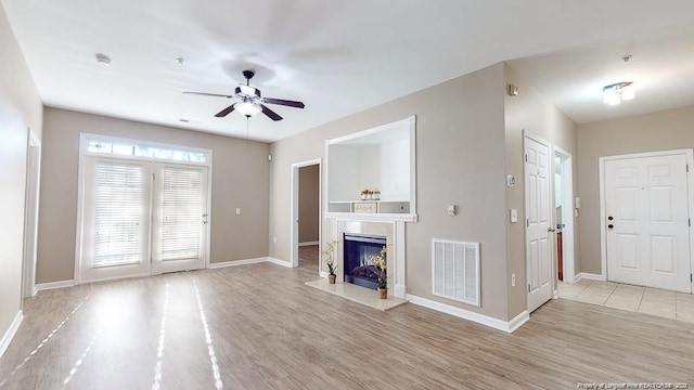 unfurnished living room with a high end fireplace, visible vents, baseboards, and wood finished floors