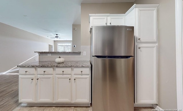 kitchen featuring ceiling fan, light stone counters, freestanding refrigerator, a peninsula, and white cabinetry