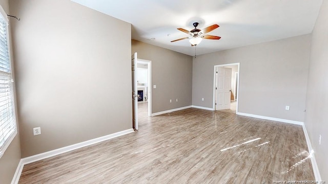 empty room with a fireplace, wood finished floors, a ceiling fan, and baseboards