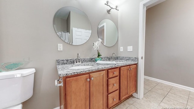 full bath featuring toilet, double vanity, a sink, and tile patterned floors