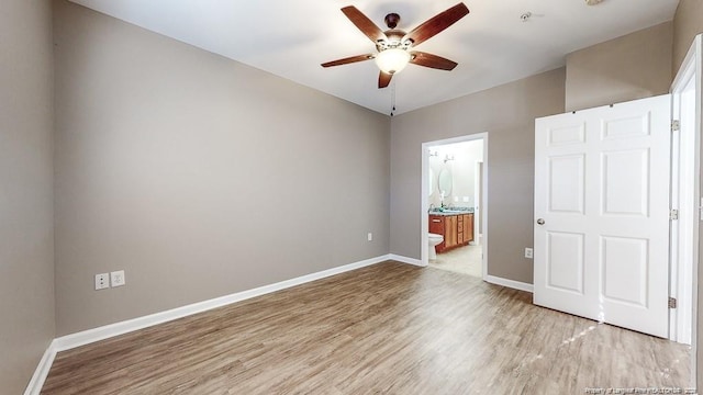 unfurnished bedroom featuring light wood-style floors, ensuite bath, baseboards, and a ceiling fan