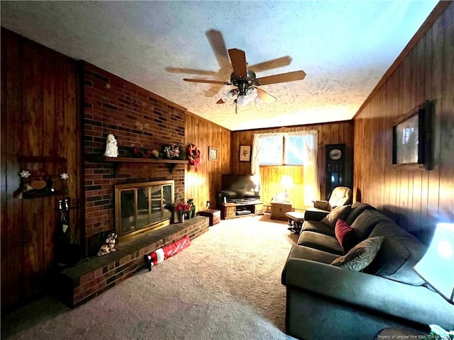 living room featuring ceiling fan, a textured ceiling, wooden walls, a fireplace, and carpet