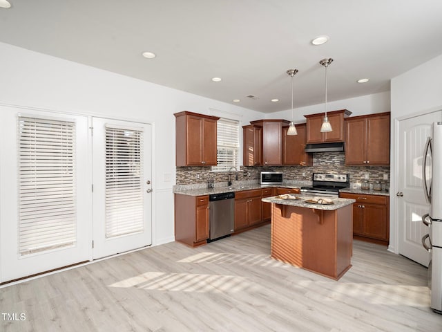 kitchen with pendant lighting, a center island, appliances with stainless steel finishes, light stone counters, and a breakfast bar area