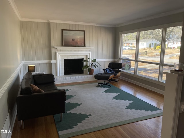 living room featuring wood-type flooring, ornamental molding, and a brick fireplace