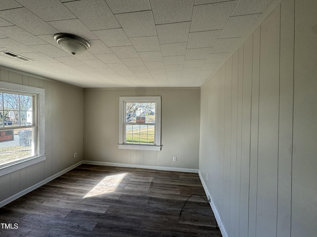 spare room with dark hardwood / wood-style floors, plenty of natural light, and wood walls