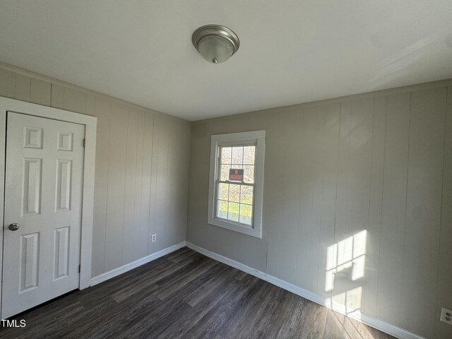 unfurnished room featuring wooden walls and dark hardwood / wood-style flooring