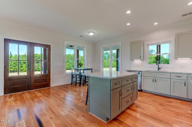 kitchen featuring light stone countertops, a center island, sink, stainless steel dishwasher, and light hardwood / wood-style floors