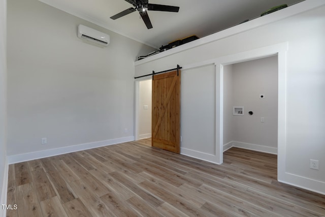 unfurnished bedroom featuring a wall mounted air conditioner, light hardwood / wood-style flooring, ceiling fan, a barn door, and ornamental molding