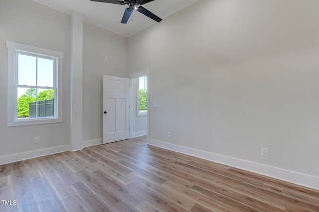 spare room featuring ceiling fan, light wood-type flooring, and a towering ceiling