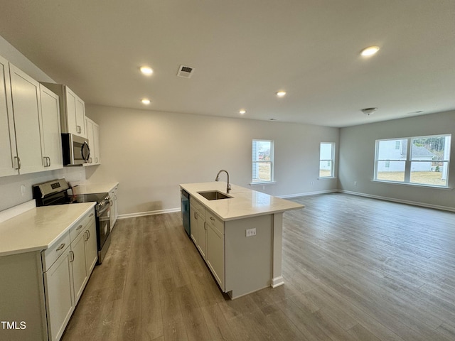 kitchen with light hardwood / wood-style floors, a kitchen island with sink, sink, and appliances with stainless steel finishes