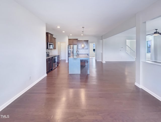 kitchen featuring dark hardwood / wood-style floors, decorative light fixtures, a breakfast bar area, a kitchen island with sink, and appliances with stainless steel finishes