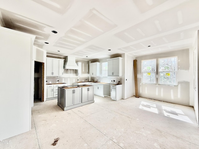 kitchen with plenty of natural light, custom range hood, white cabinets, and a center island