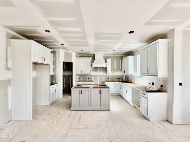 kitchen featuring a center island, custom range hood, white cabinetry, a sink, and stovetop