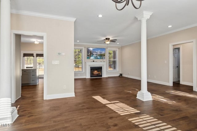 unfurnished living room featuring ceiling fan with notable chandelier, dark wood-type flooring, ornate columns, and crown molding