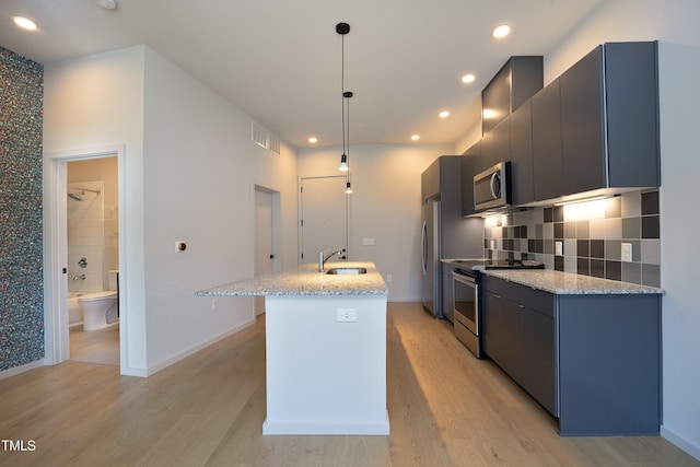 kitchen with sink, hanging light fixtures, stainless steel appliances, light hardwood / wood-style floors, and a kitchen island with sink