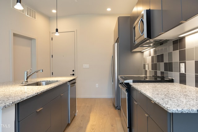 kitchen featuring light stone counters, stainless steel appliances, sink, pendant lighting, and light hardwood / wood-style flooring