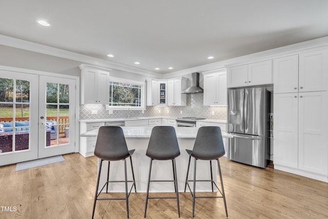 kitchen featuring french doors, wall chimney range hood, light wood-type flooring, white cabinetry, and stainless steel appliances