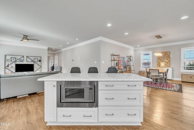 kitchen with stainless steel microwave, ceiling fan, light hardwood / wood-style flooring, white cabinetry, and hanging light fixtures