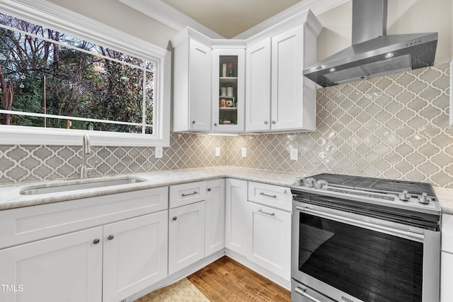 kitchen with light wood-type flooring, stainless steel range, sink, wall chimney range hood, and white cabinets