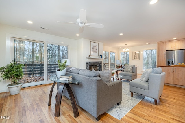 living room with a fireplace, light hardwood / wood-style flooring, and ceiling fan with notable chandelier