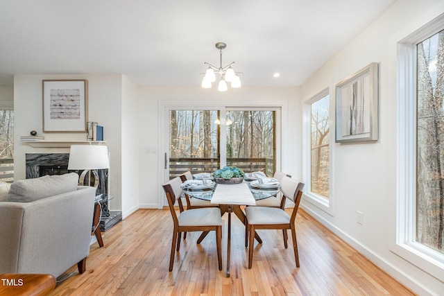 dining area with plenty of natural light, light hardwood / wood-style floors, a high end fireplace, and an inviting chandelier