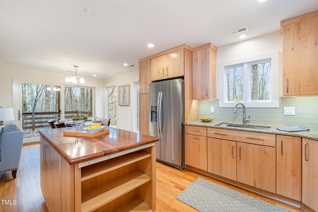 kitchen featuring sink, light brown cabinetry, decorative light fixtures, light stone counters, and stainless steel fridge with ice dispenser