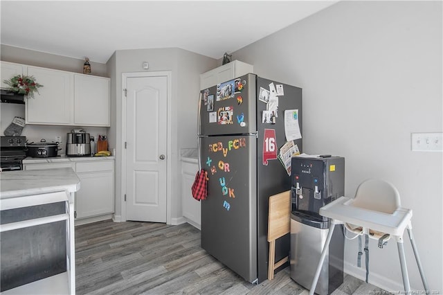 kitchen with stainless steel fridge, white cabinets, light hardwood / wood-style floors, and black range