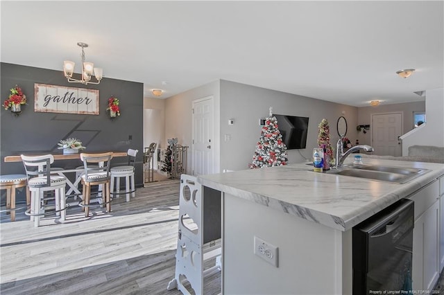 kitchen with pendant lighting, a kitchen island with sink, sink, black dishwasher, and light hardwood / wood-style floors